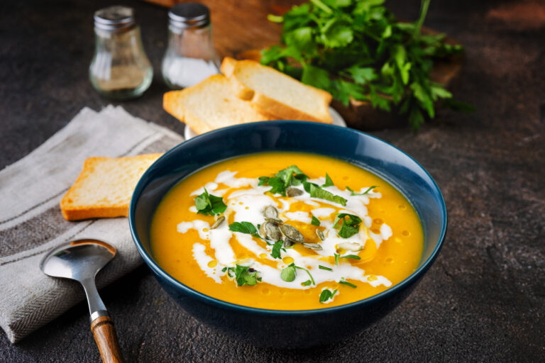 Pumpkin soup with cream and parsley on dark rustic background. Close up